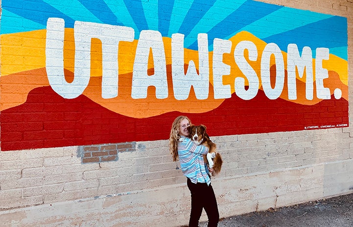 Scout the dog and woman in front of a painted Utawesome mural on the side of a building