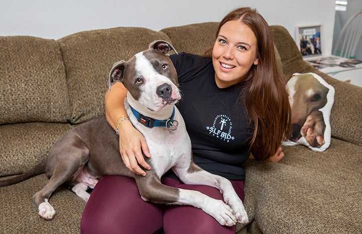 Jacqui Campos sitting on a couch with Neville the dog lying on her lap