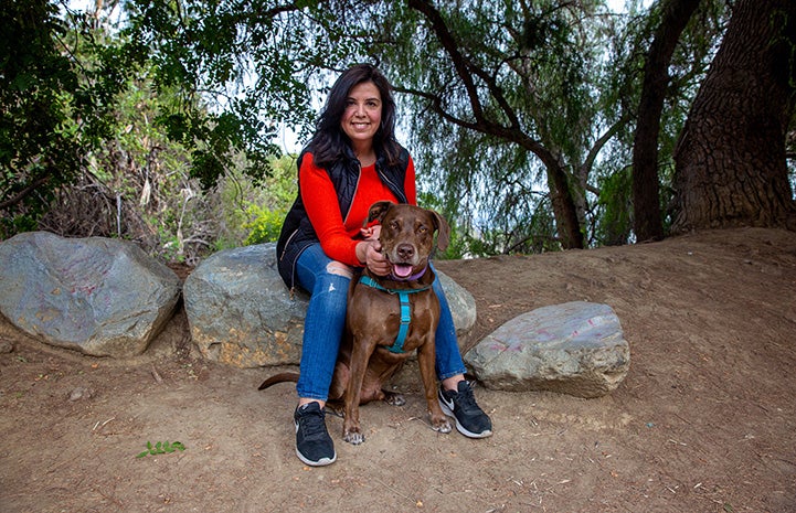 Trish Escobedo sitting on a rock with Jarvis the dog sitting in front of her