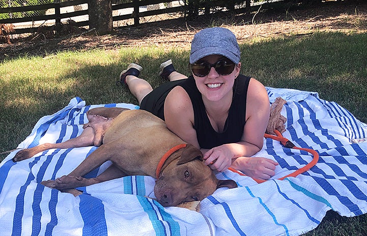 Smiling woman lying on a blanket next to Buddy the dog
