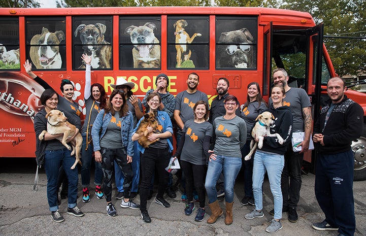 Group of people, some holding dogs, standing in front of the transport bus