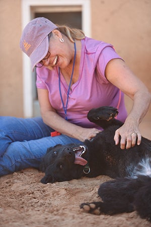 Woman smiling and sitting on the ground giving a belly rub to Rhonda the dog