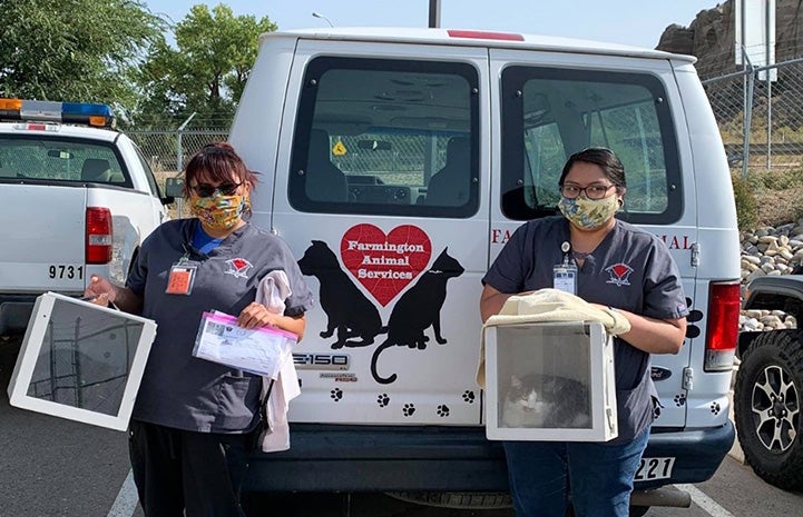 Two masked people wearing Farmington Regional Animal Shelter shirts holding boxes to hold cats, standing at the back of the shelter van