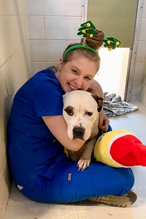 Woman wearing a holiday headband while hugging a dog in a kennel