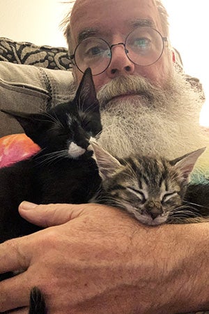 John Tindall cradling a pair of foster kittens in his arms