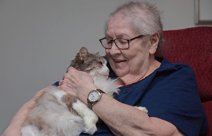 Smiling Marjory the senior woman holding Sweet Pea the cat on her lap
