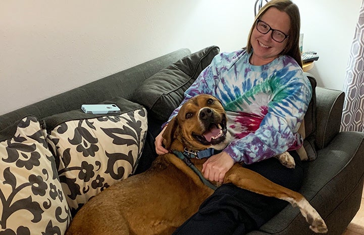 Jess the caregiver lying on a couch with Holy Moly the dog on her lap