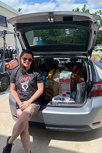 Emily Park sitting on the opened hatchback of a car that stuffed full of pet food donations