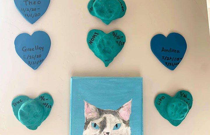 Photo of a cat painting as well as blue and teal hearts with pawprints and listed with names and dates