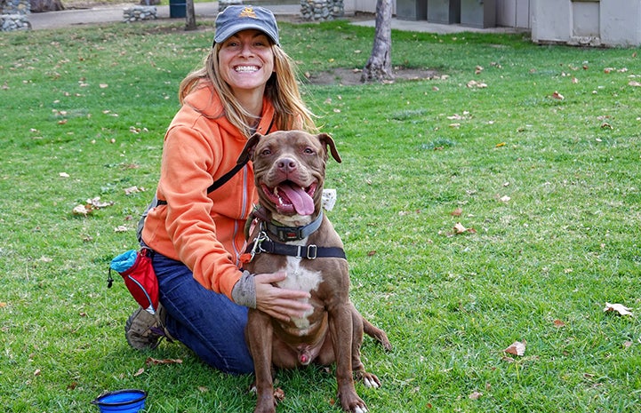 Amber Krzys, smiling and wearing a Best Friends hat, sitting on the grass next to Parker the dog