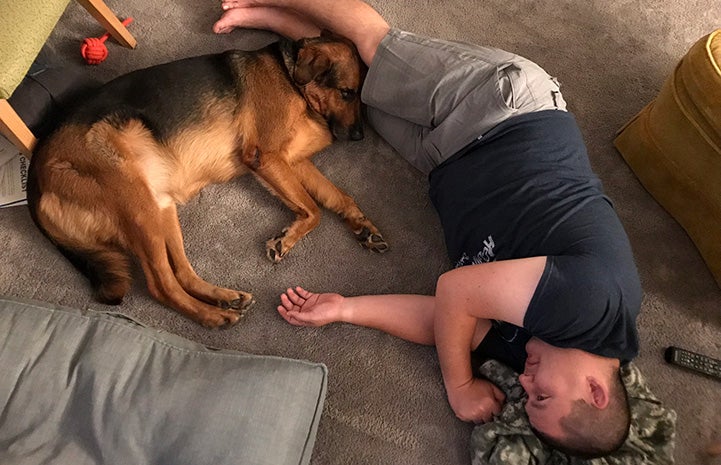 Kenny Nakanishi lying on the floor with Porter the German shepherd snuggled up next to him