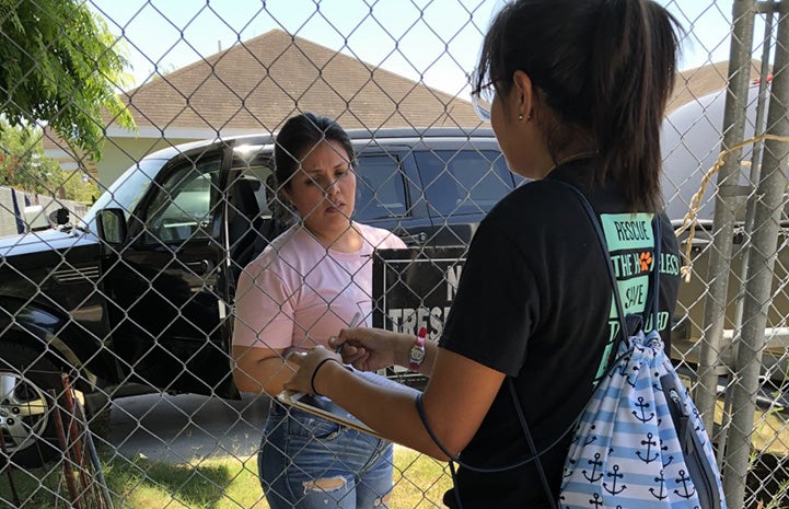 An Action Team member handing literature to another person through a chain-link fence