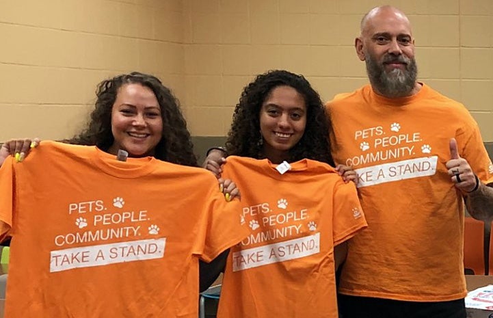 Three people with orange Best Friends Pets People Community Take a Stand T-shirts
