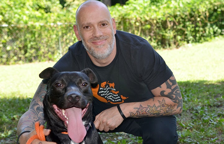 Kenny Lamberti squatting next to a black pit bull type dog whose tongue is out