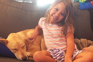 Young girl sitting on a couch next to a sleeping Harley the dog