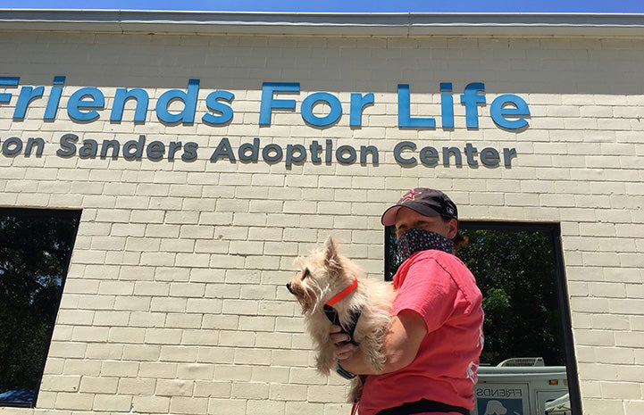 Woman holding a white fluffy dog in front of the sign on the Friends for Life adoption building