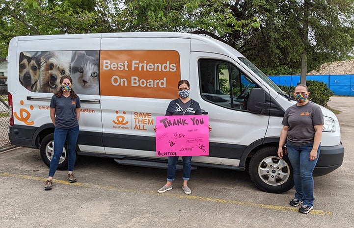 Three masked people standing in front of a Best Friends transport van with a Thank You sign