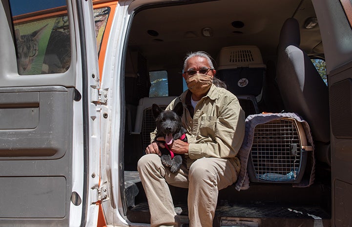 Keith Slim-Tolagai masked and sitting in the back of a van with a black dog and multiple crates