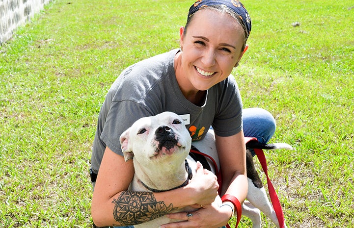 Smiling woman hugging a white pit-bull-type dog