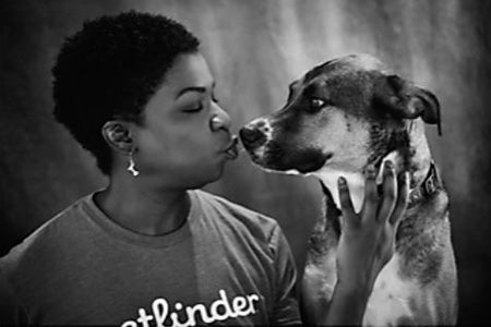 Black and white photo of Cat Small wearing a Petfinder T-shirt and kissing the nose of a dog