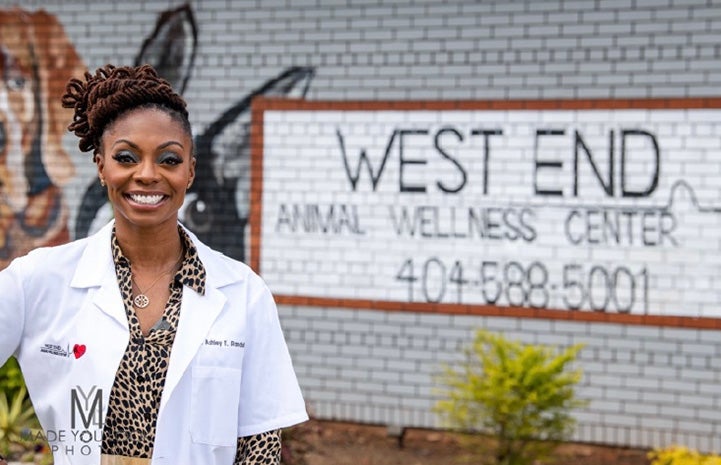 Dr. Ashley Randall, DVM standing in front of a West End Animal Wellness Center sign painted on the brick of a building