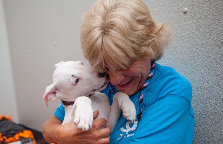 Best Friends volunteer Kathy Posekel snuggling with a white puppy
