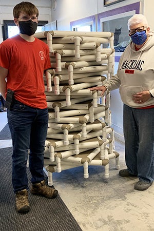 Joseph Wittke and a woman standing next to the stack of dog beds he made and donated to Amazing Grace Animal Rescue