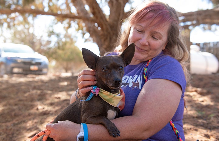 Woman holding BoPeep the dog, who is wearing a bandanna