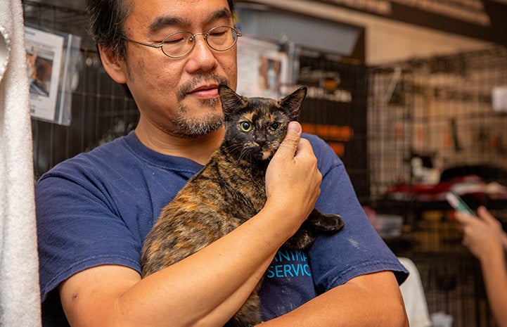Man snuggling a tortoiseshell cat close to his chest