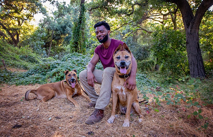 Brandon Alexander sitting in some woods with his dogs Bear and Austin