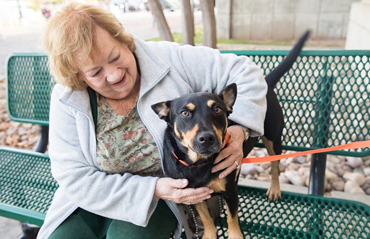 Woman sitting on a bench with a black and tan dog who she's adopting