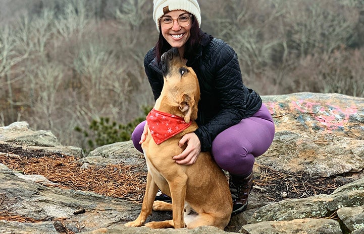 Charger the dog wearing a bandanna and looking up at the woman who adopted him while out on a hike
