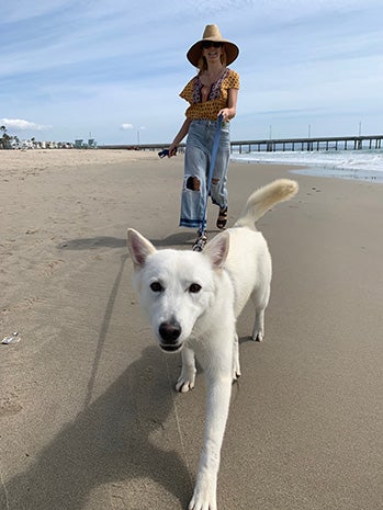 Woman wearing a hat walking Luna the dog on a leash on a beach