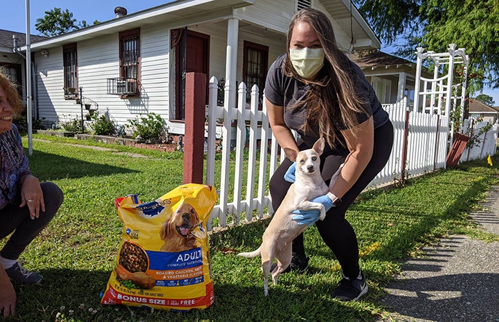 Woman wearing a mask with a small Chihuahua dog and some food she delivered