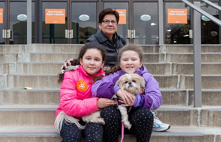 Family holding a Maltese-type dog on some steps after adopting him from the New York Super Adoption