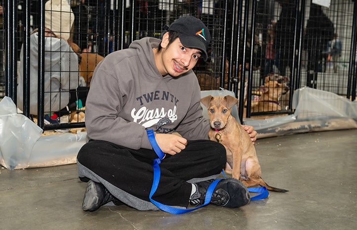 Man sitting on the ground next to a brown puppy during the New York Super Adoption