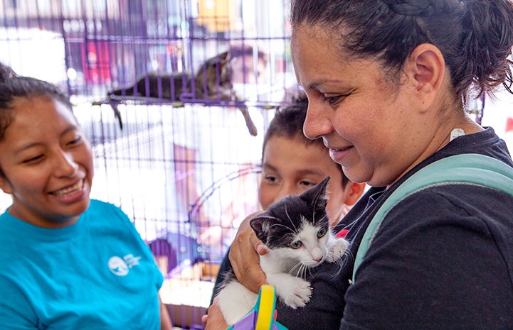 Smiling woman holding a black and white kitten while two people watch them at the New York cat adoption event