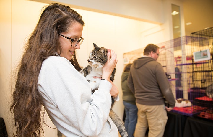 Sriracha, the brown tabby with white cat being held by a woman wearing glasses at the Save Them All Saturday in Salt Lake City