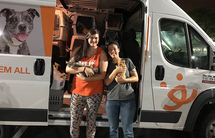 Two woman holding cats in front of the Best Friends transport van