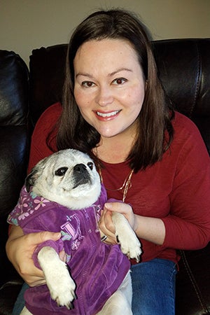 Brandy Rocchio holding Piper the pug, who is wearing a purple outfit