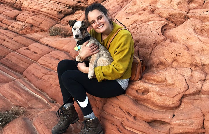Loka the puppy being held by Elise on a red rock formation