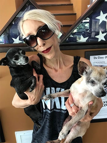 Nikki Brucato wearing sunglasses and a NKLA T-shirt, holding two small dogs