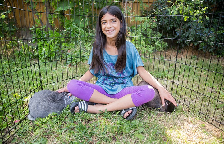A smiling Siddha Campbell with adopted rabbits Flora and Fauna