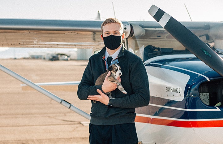 Cody Anderson holding a puppy in front of a plane