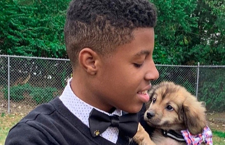 Sir Darius Brown wearing one of his bow ties and holding a small brown puppy, who is also wearing a bow tie