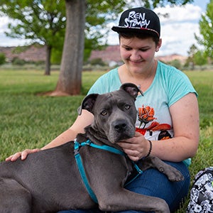 Young woman wearing a baseball hat with a gray pit bull terrier type dog
