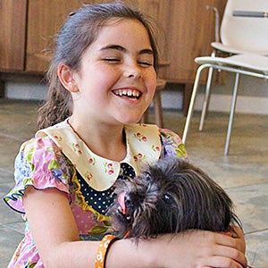 Young girl smiling and holding small furry black dog