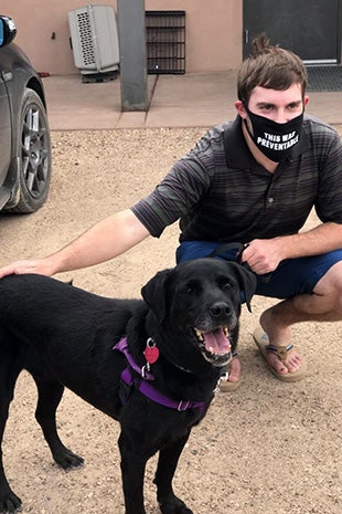 Eric wearing a mask and squatting next to Kenya the dog who is standing with a smile on her face
