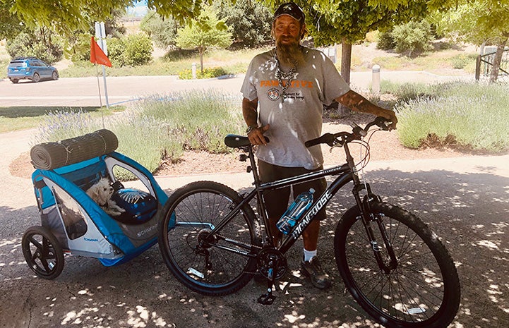 Tim Saylor with a bike that has an attached stroller containing Little Bit the dog