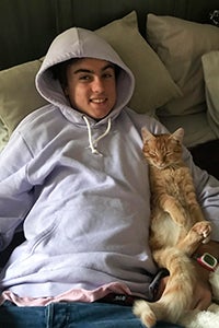 Dan the orange cat snuggling next to a boy wearing a gray hoodie